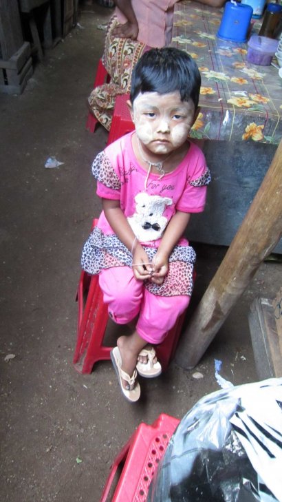 Little girl at market. She has thanaka on her face--a paste made from tree bark that is believed to protect skin from UV  rays. 